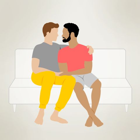 a couple sits on a couch side by side, with one arm around another, and hands touching
