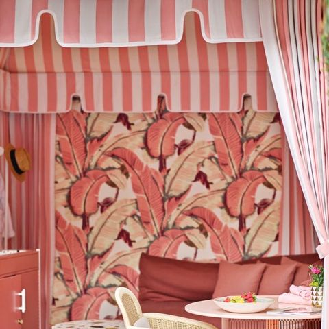 cabana seating area with reddish pink palm wallpaper matching sofa and white speckled nesting tables