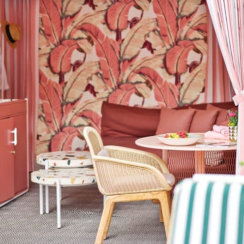 cabana seating area with reddish pink palm wallpaper matching sofa and white speckled nesting tables