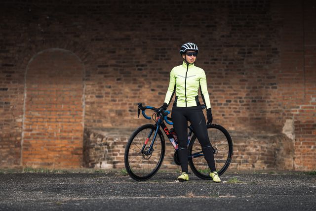wielrenster staat voor review van winter fietsjack en fietsbroek van rysel voor dames geposeerd met fiets