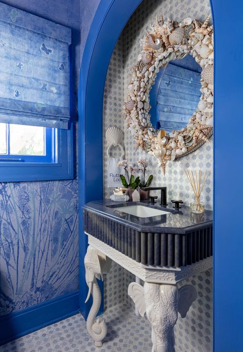 bathroom with blue trim and seashell covered round mirror above a sink with elephant shaped legs