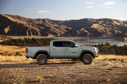 toyota tacoma parked in grassy area with mountains and a lake in the background