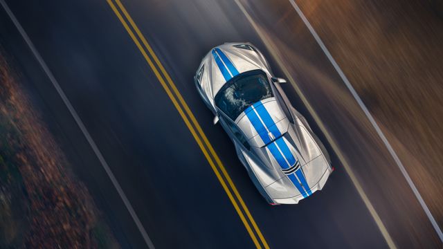 overhead view of 2024 chevrolet corvette e ray 3lz convertible in silver flare with electric blue stripe package driving on a road pre production model shown actual production model may vary model year 2024 corvette e ray available 2023