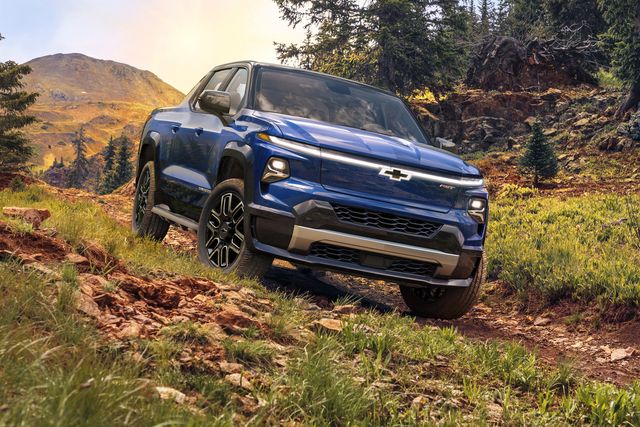 chevrolet 2024 silverado ev driving on a wooded path with trees and mountains in the background