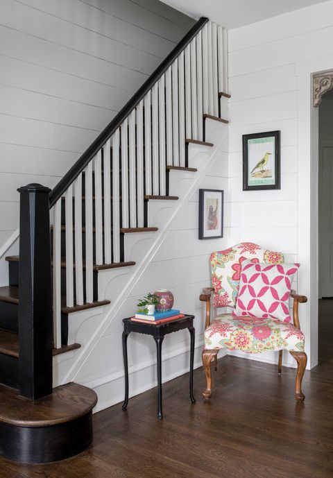 Entrance area with white and dark wooden stairs, colorful flowered chair, black side table
