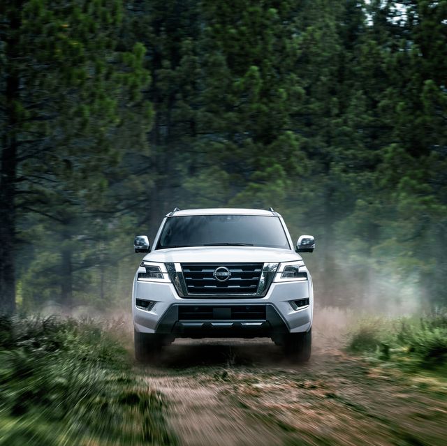 a white nissan armada driving on a dirt road surrounded by trees