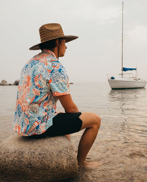 man wearing california cowboy apparel sitting on rock by water