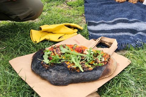 a partially burnt pizza laying on a paper bag on the ground