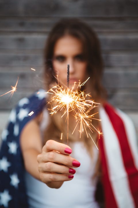 Girl holding sparklers with American flag draped over shoulder girl holding sparklers with american flag draped over shoulder