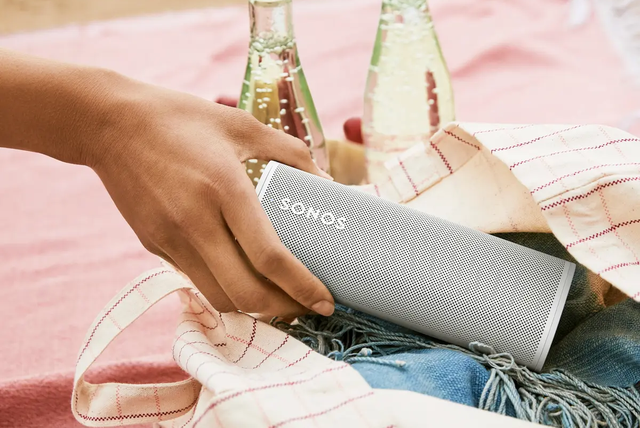 hand grabbing sonos roam from beach bag on towel in front of carbonated drinks with sand in the background