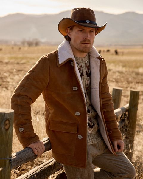 a man in a cowboy hat leaning on a fence with left leg propped up