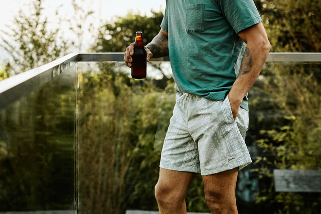 huckberry man standing on backyard deck drinking beer in bather trunk co bandana swim short