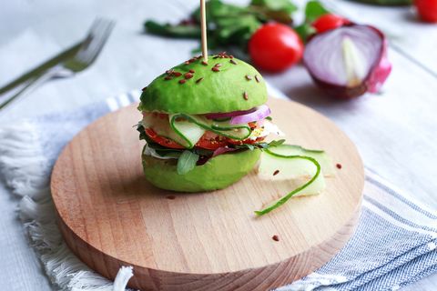 avocado burger with cucumber, tomato, onion, greens and seeds on wooden plate