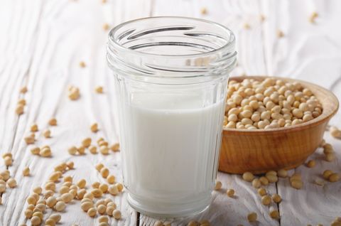 non dairy alternative soy milk or yogurt in mason jar on white wooden table with soybeans in bowl aside