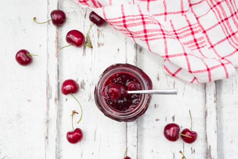 Cherries beside open jar of cherry jam on white wood