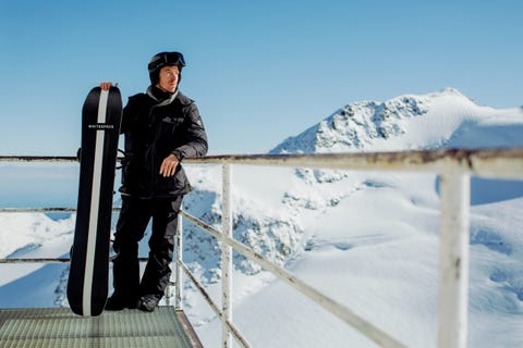 shaun white holding whitespace aspenx freestyle pro snowboard while leaning against railing looking towards the snowy mountains