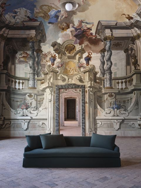 a black sofa with a large renaissance mural in the background