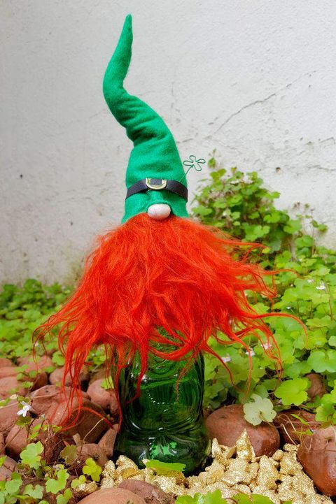 leprechaun bottle topper with bright red beard and tall green hat on top of green bottle in garden