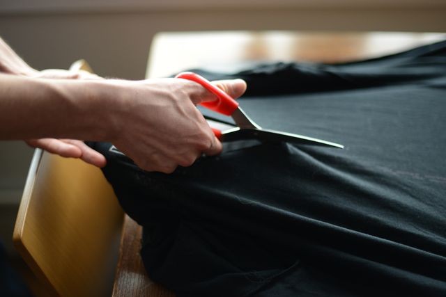 a person cutting black t shirt with a scissors