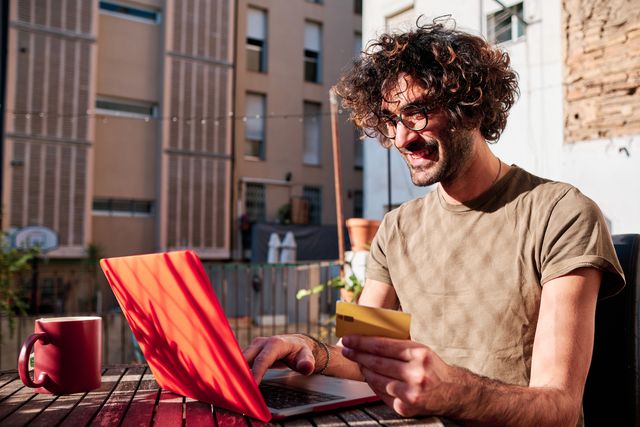 a young man buying online with his credit card and laptop at his home in a sunny day
