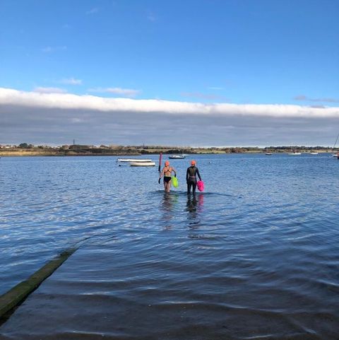 two swimmers walking out into the open water carrying buoys