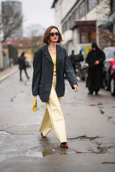copenhagen, denmark january 31 a guest wears black sunglasses, silver earrings, a silver chain necklace, a black oversized blazer jacket, a yellow ribbed wool shoulder off t shirt, a yellow matte leather handbag, pale yellow shiny leather flared pants, dark brown shiny leather pointed heels ankle shoes , outside aeron , during the copenhagen fashion week autumnwinter 2023 on january 31, 2023 in copenhagen, denmark photo by edward berthelotgetty images