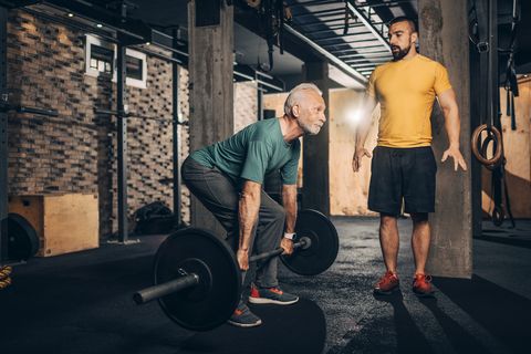 active senior male doing a deadlift exercise with his personal coach monitoring him in a gym gym