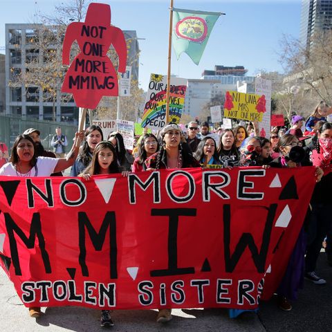 group of activists holding signs that say no more mmiw, no more stolen sisters and wearing red shirts