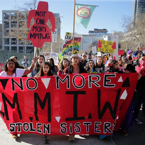 group of activists holding signs that say no more mmiw, no more stolen sisters and wearing red shirts