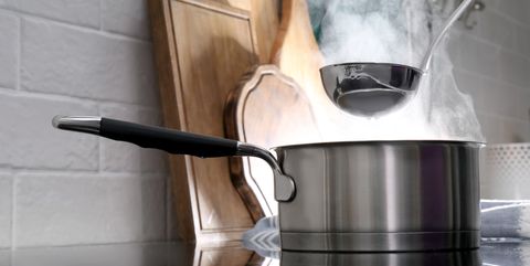 adding water with ladle into steaming saucepan on stove in kitchen