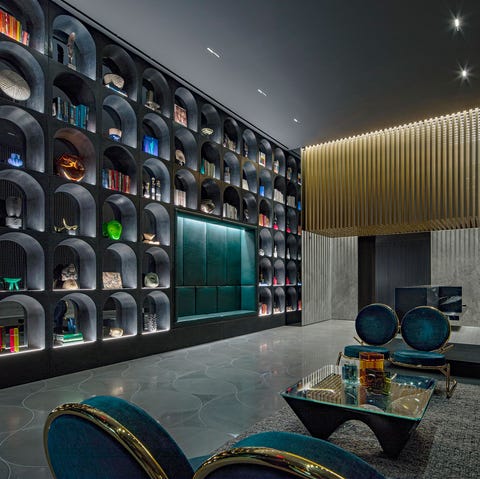 A list 2022 - ELLE DECOR moody interior with low tables and banquette along one wall and a wall of glass cubbies opposite