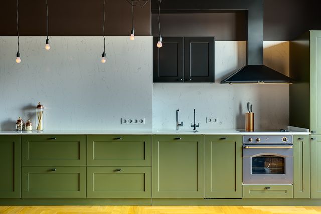 kitchen in a modern style with a light tabletop with sink, cooker, oven, kitchen accessories under tabletop there are green drawers over tabletop there is kitchen hood, cupboard and glowing lamps