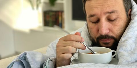 Adult man lying sick on sofa in living room eating soup with no taste