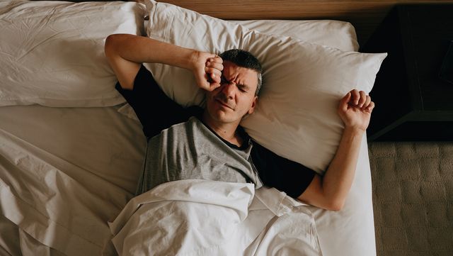 adult man waking up stretching with her arms up on her bed