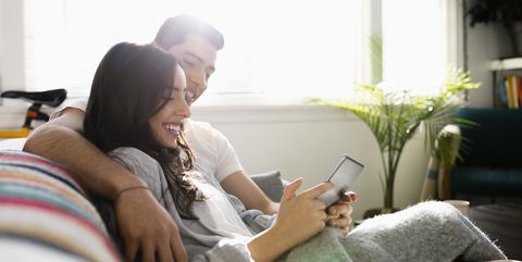 Affectionate young Latinx couple using digital tablet on living room sofa