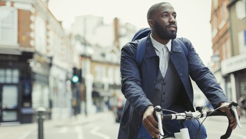 African businessman commuting, riding bicycle on urban street