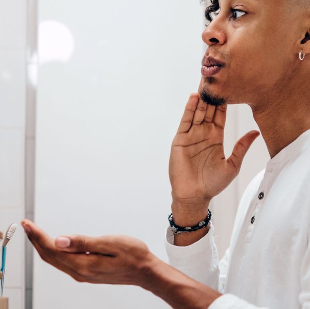 man applying aftershave while looking in bathroom mirror
