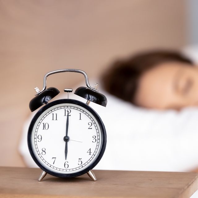 alarm clock on bedside table with woman sleeping on background