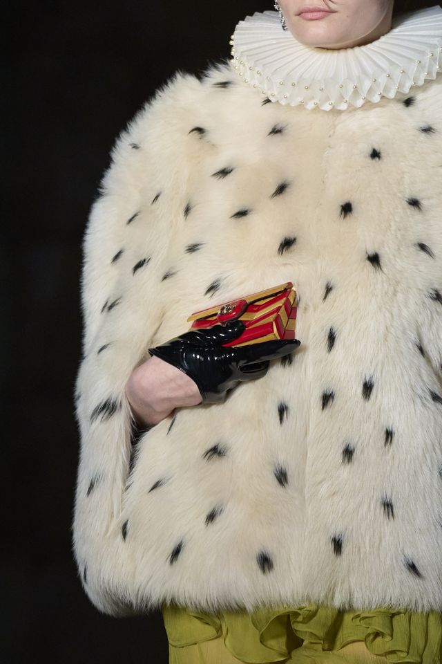 gucci close up della sfilata cosmogonie pelliccia bianca con punti neri e borsa pochette oro e rossa