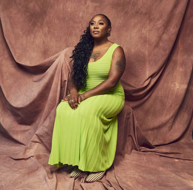 alicia garza wears a lime green dress and sits in front of a brown curtain backdrop