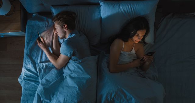 alienated millennial young couple in the bed young people turn away from each other using smartphones, browsing through social networks and not talking to each other top down camera shot