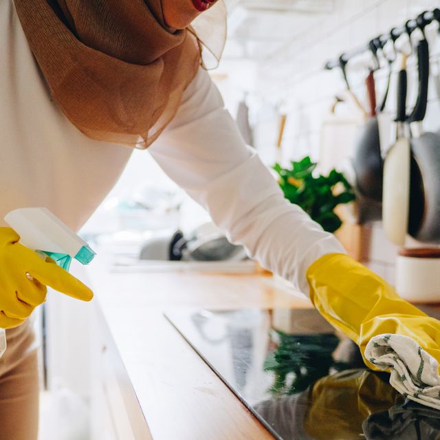 woman in yellow rubber gloves cleaning stovetop with spray bottle and rag
