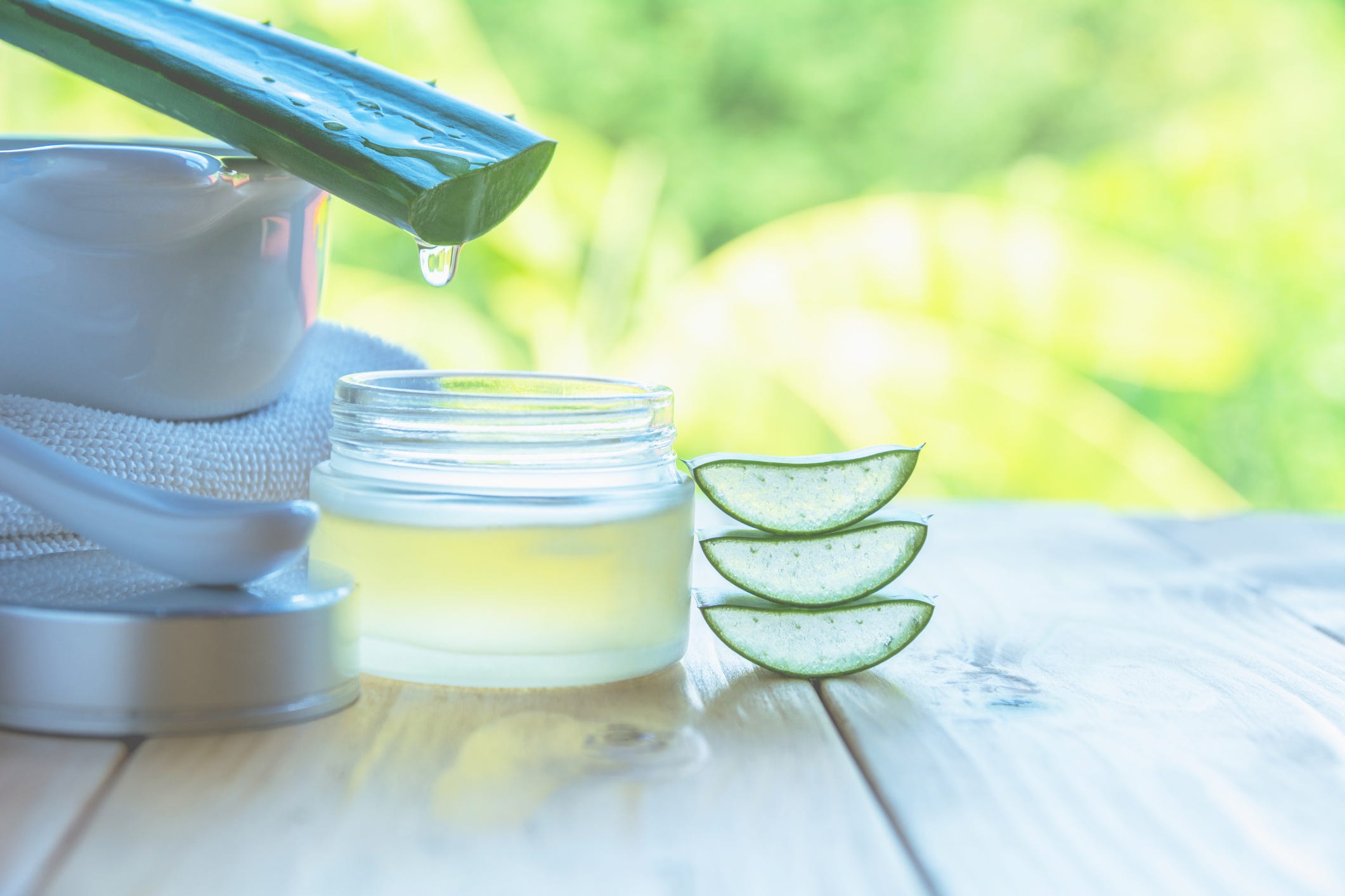 Aceite esencial de aloe vera sobre fondo natural de hojas frescas de aloe vera y vaso de zumo de aloe vera