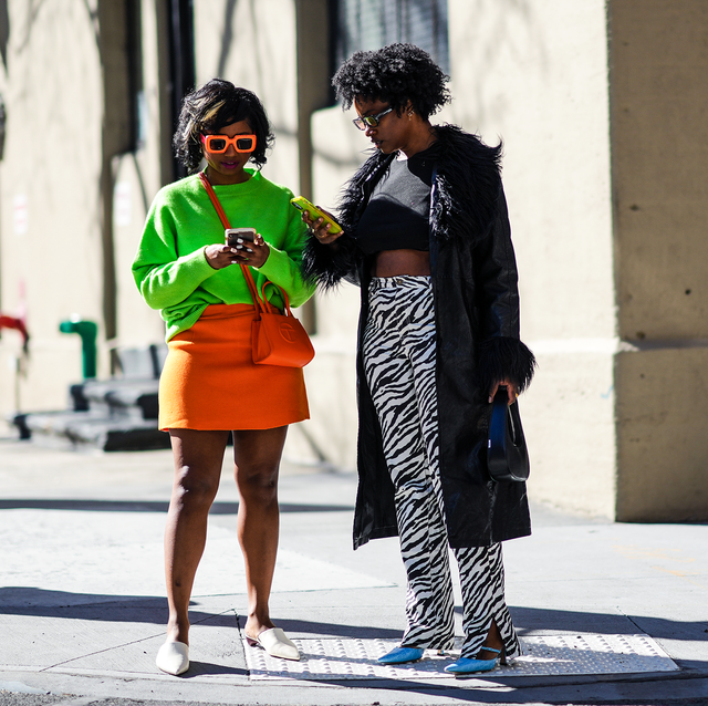 two women standing in front of a building and looking at their phones