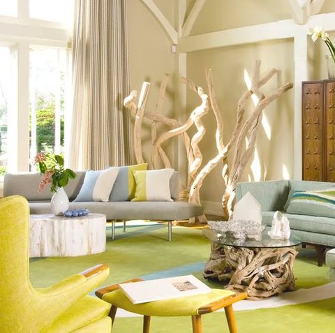 colorful living area with yellow highback chairs and asian inspired tables and a pedestal glass table with gnarled tree branches as a base as well as other art objects made from trees