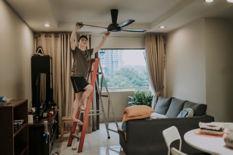 an asian chinese male cleaning ceiling fan at home