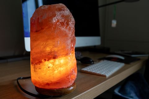 an orange pink glowing himalayan salt lamp sits on a computer desk calming concept at work