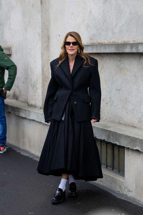 vrouw in zwarte outfit van blazer en klokrok met prada loafers en witte sokken
