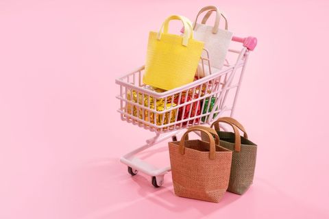 Annual sale shopping season concept - mini pink shop cart trolley full of paper bag gift isolated on pale pink background.