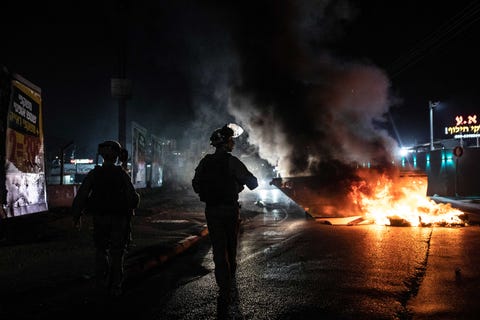 police in riot gear stand by a burning car at night